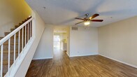 This two-story residence is designed with a functional, open layout that connects living areas seamlessly across both floors. The main level features a spacious living area with wood-look flooring, a textured ceiling, and a ceiling fan with integrated lighting. A tile-surround fireplace serves as a focal point, flanked by windows that allow natural light to filter in. A staircase with white balusters leads to the upper level, while an open passageway connects the living space to the kitchen.

The kitchen is well-equipped with white cabinetry, light countertops, a double basin sink, and black appliances including a dishwasher and electric range. A peninsula counter provides additional workspace and a visual boundary between the kitchen and adjacent areas. Vertical blinds and a window above the sink bring in additional natural light.

The upper level hosts a carpeted bedroom with a ceiling fan, a walk-in closet with built-in shelving, and access to the upper hall. Two bathrooms serve the residence — one featuring a tub/shower combination with white surround, and the other with a vanity, light countertop, and cabinetry. Wood-look flooring continues throughout the bathrooms, complementing the overall design consistency of the home.