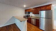 This single-floor residence in Winston-Salem, NC offers a well-organized layout with distinct living, kitchen, and bedroom areas. The open-concept living space features rich, dark hardwood-style flooring that extends from the entry door through to the kitchen area, creating a warm and cohesive aesthetic. Ceiling fans are present throughout the unit, promoting airflow and comfort in every room.

The kitchen is a standout feature, equipped with rich cherry wood cabinetry, granite countertops, and a full suite of stainless steel appliances including a refrigerator, dishwasher, range, and over-the-range microwave. A granite-topped peninsula provides additional prep space and casual seating, seamlessly connecting the kitchen to the main living area. Recessed lighting adds a polished finish to the kitchen space.

The bedrooms are finished with plush, neutral-toned carpet and feature ceiling fans and windows that allow natural light to filter in. The bathroom is appointed with a granite vanity, warm wood cabinetry, tile flooring, and chrome fixtures, including a towel bar and ring. Clean white walls and consistent trim work throughout contribute to a bright, move-in-ready atmosphere.