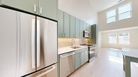 This two-story residence in Richmond, Virginia offers a thoughtfully designed layout spread across two levels. The main floor features a combined kitchen and living area with soaring ceilings that create an open, airy atmosphere. The kitchen is a standout, showcasing sage-green cabinetry with brushed chrome hardware, white quartz countertops, a subway tile backsplash, and a full suite of stainless steel appliances including a refrigerator, dishwasher, range, and microwave. Light hardwood-style flooring runs throughout, complementing the neutral warm-toned walls.

The upper level hosts the bedroom, which receives generous natural light through large windows overlooking the surrounding neighborhood. A private balcony is accessible from the upper floor, extending the living space outdoors. Two closets provide ample storage, and in-unit laundry adds everyday convenience.

The full bathroom features large-format tile, a soaking tub with shower, a green-accented vanity, and clean, modern fixtures. Recessed lighting and multiple windows ensure brightness throughout. Located along North Arthur Ashe Boulevard, this residence combines contemporary urban design with functional, well-appointed interiors.