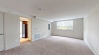 This single-floor unit offers a clean, neutral aesthetic throughout, with light-colored walls and wall-to-wall carpeting lending warmth and continuity across the main living areas. The spacious living room is a standout feature, defined by a large window that frames views of surrounding greenery and draws in generous natural light. A floor vent provides climate control, while a wall-mounted electrical panel and thermostat reflect practical, built-in conveniences. An open passageway connects the living area to the kitchen, which is outfitted with dark espresso cabinetry, light speckled countertops, a stainless steel sink, a dishwasher, and a full-size refrigerator — providing a functional and well-equipped cooking space.

The bedroom is generously proportioned, featuring its own large window with tree-lined views and dual reach-in closets with built-in shelving and hanging rods, offering substantial storage capacity. Carpeting continues throughout the bedroom, contributing to the unit's cohesive feel. The bathroom is efficiently laid out with wood-toned cabinetry beneath a white vanity countertop, a wall mirror with overhead lighting, a toilet, and a tub-shower combination set on tile flooring. The entry foyer provides a welcoming transition into the unit, completing the straightforward and functional floor plan.