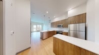 Located at 110 Roy St in Seattle's Queen Anne neighborhood, this modern one-bedroom, one-bathroom residence offers a thoughtfully designed layout with clean contemporary finishes throughout. Light hardwood-style flooring flows seamlessly across the entire space, creating a cohesive and bright atmosphere.

The open-concept kitchen is a standout feature, showcasing warm wood cabinetry, white quartz countertops, a white tile backsplash, and a full suite of stainless steel appliances including a range, microwave, dishwasher, and refrigerator. A peninsula with an integrated sink provides additional prep space and a natural divide between the kitchen and the living area. Pendant lighting and recessed fixtures illuminate the space, while a wall-mounted mini-split unit provides climate control.

The living area benefits from large windows that invite natural light and offer views of the surrounding Seattle cityscape. The bedroom is a well-proportioned retreat with a large window framing neighborhood views, accompanied by a dedicated walk-in closet outfitted with wire shelving for organized storage.

The bathroom features a long vanity with wood cabinetry, white quartz countertop, an oversized mirror, and a full soaking tub with a tiled surround. Clean white walls and modern hardware complete the polished, minimalist aesthetic throughout this efficiently designed Seattle residence.