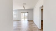 This single-story home offers a thoughtfully designed layout across three bedrooms, two bathrooms, and a combined living and kitchen area. Wood-look tile flooring flows consistently throughout the home, complementing the bright, white walls and clean crown molding details that define each room.

The open living area is expansive and filled with natural light, drawing the eye toward a sliding glass door that opens to a balcony with panoramic views of the surrounding landscape and distant cityscape. Track lighting and multiple windows further enhance the airy atmosphere.

The kitchen is well-equipped, featuring white cabinetry, dark granite countertops, a tile backsplash, and stainless steel appliances including a refrigerator, range, and microwave. A peninsula provides additional counter space and casual seating potential.

The generously sized primary bedroom includes a ceiling fan, natural light from a side window, and direct access to a walk-in closet outfitted with dual hanging rods and shelving. Additional bedrooms are bright with large windows. The bathrooms feature dark granite vanities, white cabinetry, mosaic tile accents, and glass-enclosed showers with marble-style tile surround.