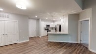 This single-floor residence in Greensboro, NC, offers a clean, contemporary design throughout its open layout. The main living area flows directly into the kitchen, which serves as a functional centerpiece of the space. White shaker-style cabinetry extends to the ceiling, complemented by a subway tile backsplash, light granite countertops, and a full suite of stainless steel appliances including a French door refrigerator, electric range, and built-in microwave. A peninsula with an integrated sink and pendant lighting overhead provides additional workspace and separates the kitchen from the living area. Wood-look plank flooring runs throughout the main living spaces, adding warmth and continuity.

A carpeted hallway connects the private areas of the unit, including multiple bedrooms, each fitted with plush carpet, natural light from double windows, and ceiling fans. The primary bathroom features a walk-in shower, a dual-sink vanity with granite countertops, and direct access to a walk-in closet with built-in shelving. A secondary bathroom mirrors the refined aesthetic with a granite-topped vanity and a tub-shower combination. Neutral gray tones and recessed lighting maintain a cohesive, modern ambiance throughout.
