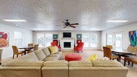 Located at 922 N Sidney Ave in Russellville, Arkansas, this single-floor space offers a well-organized open-concept layout that combines the kitchen and living area into one cohesive environment. The living room is a welcoming focal point, anchored by a white brick fireplace with a mounted television above the mantle. Large windows and multiple sets of glass patio doors line the walls, flooding the space with natural light and offering views of the outdoor surroundings, including a glimpse of a pool area. A ceiling fan overhead and textured ceilings add to the room's character, while recessed skylights further brighten the interior. A dedicated dining area sits near the patio doors, complemented by a vibrant piece of wall art that adds a splash of color. The kitchen features white cabinetry, tile flooring, and ample counter space, with black appliances including a range and over-the-range microwave. A breakfast bar with bar seating provides a casual dining option and serves as a natural divider between the kitchen and the adjacent living space. The overall ambiance is bright, open, and functional, with neutral tones throughout that create a versatile and inviting atmosphere.