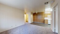 Located at Village Center Drive in Sacramento, CA, this 2-bedroom, 1-bathroom single-floor home offers a practical and comfortable layout. The open living area flows directly into the kitchen, creating a connected and functional space. The kitchen features warm oak-toned cabinetry, a full-size refrigerator, a dishwasher, a stove, and a stainless steel sink with light countertops, all set on wood-look vinyl flooring. A striking wall of floor-to-ceiling wood-panel cabinetry serves as a defining architectural feature between the living and kitchen areas, providing generous storage. The living area is finished with plush carpet and equipped with track lighting overhead. Both bedrooms are carpeted and bathed in natural light through large windows dressed with vertical blinds. The primary bedroom includes a dedicated closet area, while the second bedroom features sliding mirrored closet doors. The full bathroom is finished with wood-look vinyl flooring, a tub-shower combination with safety grab bars, and clean, neutral-toned walls. A utility room and additional closet space round out the home's practical offerings. The overall aesthetic is clean, neutral, and move-in ready.