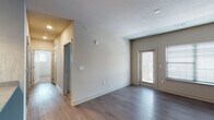 This single-floor unit presents a clean, modern design with a well-considered layout connecting living, kitchen, and bedroom spaces. The open living area features wood-style plank flooring, neutral-toned walls, and a glass-paneled entry door alongside a window fitted with blinds, allowing natural light to fill the space comfortably.

The kitchen is a standout feature, equipped with dark espresso cabinetry, white quartz-style countertops, a tile backsplash, and a full suite of stainless steel appliances including a refrigerator, electric range, and built-in microwave. A central island with an undermount sink and pendant lighting above adds both functionality and visual appeal. Recessed lighting illuminates the space effectively.

The bedrooms are carpeted in neutral tones and include windows with blinds that provide natural light. A ceiling fan is present in one bedroom, adding comfort and airflow.

The bathroom is finished with wood-style flooring, a single undermount sink set in a quartz-style vanity with dark cabinetry, a large mirror, and a full tub-shower combination with white tile surround. The overall aesthetic throughout the unit is cohesive, contemporary, and well-appointed.
