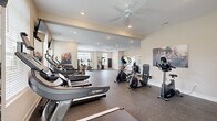 Located at 166 Caldy Knoll Dr in Sunbury, Ohio, this fitness center offers a generously sized, single-floor layout designed to accommodate a comprehensive range of workout activities. The space features a durable rubber-composite flooring that provides cushioning and traction throughout, making it well-suited for both cardio and strength training exercises.

The cardio section is prominently outfitted with multiple Spirit-brand treadmills arranged in a row, complemented by elliptical trainers and stationary bikes. Flat-screen televisions are mounted at eye level along the treadmill row, enhancing the workout experience. A dedicated strength training area includes a cable/multi-functional machine, a rack of dumbbells, and a weight bench, providing options for a full-body workout routine.

The space benefits from abundant natural light streaming through multiple large windows fitted with blinds, creating a bright and motivating atmosphere. Ceiling fans with recessed lighting maintain air circulation and comfort throughout. Large mirrors are positioned along one wall, expanding the perceived depth of the room. Motivational fitness artwork decorates the neutral-toned walls, contributing to an energetic yet clean aesthetic. The open floor plan allows for ample movement between equipment stations.