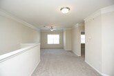 This single-floor residence presents a cohesive, neutral-toned interior highlighted by crown molding and ceiling fans throughout. The expansive living area features plush wall-to-wall carpeting and flows into a long hallway corridor with natural light filtering through a window at the far end. A half-wall partition subtly divides the living space from the kitchen area.

The kitchen is outfitted with warm honey-toned cabinetry, dark laminate countertops, and a full suite of black appliances, including an electric range, dishwasher, and over-the-range microwave. Crown molding carries through into the kitchen, maintaining design consistency across the space.

The bedrooms are generously sized, each featuring soft carpeting, ceiling fans, crown molding, and large windows that bring in natural light. One bedroom includes a walk-in closet with wire shelving and an additional standard closet, providing ample storage.

The bathroom is cleanly appointed with tile flooring, a tub-shower combination featuring a black and white tile accent border, a dark countertop vanity, and warm wood cabinetry. A dedicated laundry nook accommodates a full-sized washer and dryer with an overhead wire storage shelf, adding practical functionality to the unit.