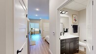 This thoughtfully designed single-floor unit offers a modern aesthetic with a clean, neutral palette throughout. Light-toned hardwood flooring runs continuously across the space, connecting each area seamlessly while recessed lighting ensures a bright, welcoming atmosphere.

The kitchen is efficiently laid out, featuring dark lower cabinetry paired with white upper cabinets, quartz countertops, a stainless steel sink, a full-size refrigerator, and a classic white subway tile backsplash — a stylish contrast that defines the culinary space.

The living area provides a comfortable retreat, highlighted by a tall window that invites natural light and frames the room with a sense of openness. The bedroom is intimate and well-proportioned, offering a sliding-door closet, soft neutral walls, and ample room for restful living.

The bathroom is finished with a dark espresso vanity, a crisp white countertop, bold matte black fixtures, a large wall mirror, and a walk-in shower with matte black hardware. Notably, a stacked Whirlpool washer and dryer unit is tucked conveniently within the bathroom area, adding practical in-unit laundry access.

Overall, the unit presents a cohesive modern design with quality finishes, efficient use of space, and functional amenities suited for contemporary living.
