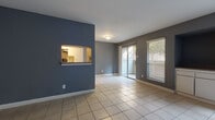 This single-floor space is designed with a practical, open layout that makes efficient use of every area. The main living space is finished with large neutral ceramic tile flooring that extends throughout the unit, providing a cohesive and easy-to-maintain surface. The walls are painted in a contemporary slate gray palette, lending a modern, understated character to the interior.

The living area is bright and airy, benefiting from natural light streaming through a sliding glass door that opens directly onto a private outdoor patio with a wooden slat privacy fence. An additional window with horizontal blinds further enhances the natural light.

A standout architectural feature is the pass-through window cut into the accent wall, connecting the living area to the kitchen. The galley-style kitchen is outfitted with white cabinetry, speckled countertops, a subway tile backsplash, a stainless steel sink, and black appliances including a refrigerator, range, and dishwasher.

The bedroom offers a comfortable retreat, complete with a ceiling fan, a window with natural light, and a sliding-door closet. The bathroom features a large vanity with white cabinetry, speckled countertops, a wide mirror, and a separate water closet, all finished with the same light tile flooring found throughout the space.