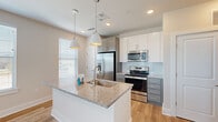 Located at 3229 W Montague Ave in North Charleston, SC, this thoughtfully designed one-bedroom, one-bathroom unit offers a clean, modern aesthetic across a single floor. The open-concept kitchen and living area serves as the heart of the home, anchored by a large center island with granite countertops and an undermount sink, illuminated by stylish pendant lights. White upper cabinetry is complemented by gray lower cabinets, while a subway tile backsplash and full suite of stainless steel appliances — including a french door refrigerator, range, and microwave — complete the kitchen. Light hardwood-style flooring flows throughout the main living areas, adding warmth and continuity. The living room features a ceiling fan, multiple windows with blinds, and glass French doors that invite natural light and provide outdoor access. The bedroom is finished with plush carpet, a ceiling fan, and a window with views of the surroundings. The bathroom offers a dual-sink vanity with granite countertops set in teal cabinetry, a large mirror, and a tub-shower combination. An entry hallway includes built-in shelving and a closet, providing functional storage from the moment you walk in.