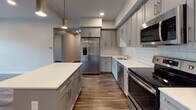 Located at 1 Marys Way in Lincoln, Massachusetts, this single-floor residence offers a thoughtfully designed open-concept layout with modern finishes throughout. The main living and dining area is anchored by rich wood-look flooring, recessed lighting, and a cassette-style HVAC unit, creating a clean and comfortable atmosphere that flows seamlessly into the kitchen.

The kitchen is a standout feature, equipped with grey shaker-style cabinetry, white subway tile backsplash, light quartz countertops, a large center island, and a full suite of stainless steel appliances including a French door refrigerator, range, built-in microwave, and dishwasher. A convenient walk-in pantry closet is situated just off the kitchen.

The bedrooms are finished with plush carpeting and feature vaulted ceiling lines that lend architectural character to each room. Windows throughout provide views of the surrounding greenery, filling the spaces with natural light. Bedroom closets offer generous storage capacity.

The bathroom is finished with light tile flooring, a dark wood vanity with quartz countertop, a large mirror, and a full tub-shower combination with white tile surround. In-unit laundry with a stacked washer and dryer adds everyday convenience, accompanied by additional closet storage nearby.