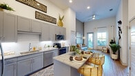 This efficiently designed 2-bedroom, 1-bathroom residence makes a strong architectural impression through its notably high ceilings, which create a sense of openness throughout the single-floor layout. The open-concept kitchen is a standout feature, outfitted with gray shaker-style cabinetry, granite countertops, a white subway tile backsplash, and a full suite of stainless steel appliances including a range, microwave, and dishwasher. A central island with a granite surface and seating for two serves as both a functional workspace and casual dining area.

The living room benefits from soaring ceiling heights, large windows, and a glass door providing outdoor access and abundant natural light. Light-toned hardwood-style flooring runs throughout the main living areas, enhancing the airy feel.

The primary bedroom features warm-toned walls, elevated ceilings, a large window, and dedicated closet space. The second bedroom offers a similarly comfortable layout. The shared bathroom is finished with wood-look tile flooring, granite vanity surfaces, and a glass-enclosed shower with white tile surround. The overall design balances modern finishes with a warm, welcoming ambiance throughout.