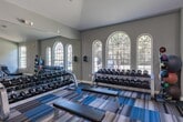 Located at 29980 FM-2978 in Magnolia, Texas, this fitness center offers a comprehensive workout environment designed to accommodate a wide range of exercise routines. The single-floor facility is generously proportioned, providing ample space between equipment for comfortable movement throughout the room.

The interior features soft blue-gray walls and a distinctive striped carpet in shades of blue, tan, and gray, lending the space a clean, modern aesthetic. Ceiling fans and flush-mounted fluorescent lighting ensure the room remains well-lit and well-ventilated during use. Large arched and rectangular windows along the perimeter walls invite abundant natural light and offer views of the surrounding outdoors.

The cardio section is well-stocked with treadmills, elliptical trainers, stationary bikes, and recumbent cycles, all arranged for ease of access. The strength training area features a comprehensive selection of cable machines, multi-function cable stations, free weight benches, and a full dumbbell rack, accommodating both beginner and advanced lifters. Full-length mirrors line portions of the walls, enhancing the sense of space and allowing users to monitor their form. A wall-mounted television adds an entertainment option for cardio sessions. French doors at one end of the facility provide direct access to the outdoors, further connecting the space to its natural surroundings.