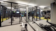 This contemporary fitness center is thoughtfully designed to accommodate a wide range of workout routines across multiple functional zones. The space is anchored by a striking yellow and gray modular flooring system that visually delineates different training areas while adding a vibrant, energetic aesthetic throughout.

The cardio zone features a row of Matrix treadmills positioned along floor-to-ceiling glass garage-style doors, which open to allow natural light and views of the surrounding urban environment. Mounted monitors provide entertainment and connectivity for users during workouts. Adjacent to this area, a selection of elliptical trainers and upright exercise bikes offers varied low-impact cardiovascular options.

A dedicated strength and free weights section houses a dumbbell rack, cable machines, and additional resistance equipment, all arranged to maximize floor space and usability. Ceiling-mounted fans ensure consistent airflow across the open training floor.

A glass-walled studio room provides a semi-private space ideal for cycling classes, stretching, or personal training sessions. It is outfitted with spin bikes, a flat bench, stability balls, and wall-to-wall mirrors that amplify the sense of space and support form monitoring. The industrial-style exposed ceiling with linear lighting fixtures adds a modern, urban character to the overall environment.