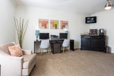 Located at Woodland Pointe in Nashville, Tennessee, this single-story community space is thoughtfully designed to offer residents and visitors a comfortable and functional environment. The interior showcases classic architectural details, including crown molding, arched doorways, and soaring ceilings that lend a sense of openness and refinement throughout.

The main gathering area features plush carpeting, a ceiling fan, and generous natural light streaming through large windows with white blinds, creating a bright and inviting atmosphere. Stylish seating arrangements make this space ideal for relaxed conversation or quiet contemplation.

A dedicated business center provides workstations equipped with computers, a printer, and ample desk space, accented by contemporary artwork on the walls. Adjacent to this is a lounge and refreshment area furnished with a bistro-style table and stools, a wall-mounted television, and a beverage station atop a dark wood credenza — perfect for informal gatherings.

Glass-paneled French doors with bold dark frames elegantly connect the various areas, while hardwood and carpeted flooring guide the transition between spaces. A chandelier adds a classic touch to the connecting corridor, complementing the overall refined aesthetic. The cohesive design throughout balances functionality with welcoming warmth, making this a standout community facility.