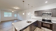 Located at 25100 Ashton Cir in Frankford, Delaware, this single-floor, 3-bedroom, 2-bathroom home offers a thoughtfully designed layout with clean, modern finishes. A welcoming hallway with light wood-look flooring leads into the open-concept living, dining, and kitchen area, where natural light flows through windows framed with white blinds. The kitchen is a standout feature, showcasing dark shaker-style cabinetry, granite countertops, a large peninsula with a built-in sink and dishwasher, elegant pendant lighting, and a full suite of stainless steel appliances. The living area is complemented by a ceiling fan overhead. Each of the three bedrooms continues the light wood-look flooring and clean white walls, with ceiling fans and windows providing ventilation and natural light. Several bedrooms include closets, with one featuring a spacious walk-in closet outfitted with wire shelving. The two bathrooms are bright and modern, including a walk-in glass shower. A dedicated laundry room houses a full-size washer and dryer with additional wire shelving above. Five closets throughout the home provide generous storage. The overall ambiance is clean, bright, and move-in ready.
