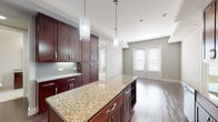 This thoughtfully designed single-floor residence offers a cohesive blend of modern finishes and functional living spaces. The centerpiece of the home is a gourmet kitchen outfitted with rich dark wood cabinetry that extends to the ceiling, providing generous storage throughout. A large central island with a granite countertop serves as both a workspace and a gathering point, illuminated by stylish pendant lighting overhead. The kitchen is equipped with a full suite of stainless steel appliances, including a French door refrigerator, electric range, and over-the-range microwave. A subway tile backsplash adds a refined touch, complementing the warm hardwood flooring that flows through the main living areas. The open layout connects the kitchen seamlessly to the living space, which features French doors that invite natural light and offer access to the exterior. The bedrooms are finished with plush carpeting and feature multiple windows with exterior views, creating bright and comfortable retreats. The bathrooms are appointed with large-format tile flooring, dark wood vanities topped with granite countertops, framed mirrors, and a tiled tub-shower combination, maintaining the consistent upscale aesthetic found throughout the rest of the home.