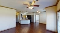 This well-appointed 2-bedroom, 2-bathroom single-floor residence in Montgomery, Texas offers a thoughtfully designed open-concept layout that seamlessly connects the living, dining, and kitchen areas. Rich, dark hardwood flooring flows throughout the main living spaces, adding warmth and visual continuity, while a ceiling fan with integrated lighting anchors the spacious living area. Crown molding provides an elegant finishing touch along the upper walls.

The kitchen is a functional centerpiece, featuring an angled peninsula with a granite-style countertop, a stainless steel sink, and pendant lighting overhead. Dark espresso cabinetry contrasts smartly with the light countertops, and black appliances — including a refrigerator, range, and microwave — complete the suite. A breakfast bar configuration makes the kitchen ideal for both cooking and casual dining.

The primary bathroom includes a double-sink vanity with dark cabinetry, a large framed mirror, and ample counter space. The second bathroom offers a full tub and shower combination with classic tile accents. Both bedrooms are carpeted and receive natural light through large windows with outdoor views of the surrounding landscape. Built-in shelving and generous closet space add practical storage options throughout the home. A private entry door with sidelight window completes this inviting residence.