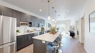 This efficiently designed one-bedroom, one-bathroom unit offers a thoughtful single-level layout that maximizes its compact footprint. The open-concept kitchen and living area serves as the heart of the unit, featuring light wood-style flooring that flows throughout the main living spaces. The kitchen is outfitted with dark wood-tone cabinetry extending to the ceiling for ample storage, paired with white quartz countertops, a full suite of stainless steel appliances including a refrigerator, dishwasher, microwave, and range, and a peninsula that provides additional prep and dining space. Pendant lighting above the peninsula adds a modern design touch. The living area is bright and airy, benefiting from a large sliding glass door that fills the space with natural light and offers views of the surrounding landscape. The bedroom, finished with plush carpeting, features a window with outdoor views and dedicated closet storage. The bathroom connects conveniently between the living and sleeping areas and includes dark cabinetry with light countertops, consistent with the unit's cohesive modern aesthetic. Neutral wall tones throughout contribute to a clean, open ambiance.