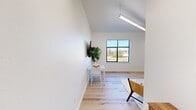 Located at 2600 College Ave in Conway, Arkansas, this thoughtfully designed one-bedroom, one-bathroom unit delivers a clean, modern aesthetic across a single floor. The open living area immediately impresses with its soaring vaulted ceiling, a sleek pendant light fixture, and a large window that frames outdoor views while flooding the space with natural light. Light-toned hardwood-style flooring runs throughout, lending warmth and cohesion to the interior. The living area comfortably accommodates a seating arrangement and benefits from a wall-mounted television, creating a functional yet stylish gathering space. A compact kitchen area is positioned conveniently nearby. The generously sized bedroom is bathed in natural light courtesy of large floor-to-ceiling windows with views of the surrounding area, and features soaring walls that enhance the sense of openness. The bathroom is clean and efficiently laid out, featuring a shower-tub combination with a curtain enclosure, a single vanity, and tasteful artwork on the walls. Throughout the unit, the crisp white walls, consistent flooring, and minimalist design elements create a bright, airy ambiance well-suited for comfortable everyday living.
