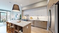 This well-appointed 1-bedroom, 3-bathroom residence offers a refined urban living experience within a compact yet efficiently designed single-floor layout. Light hardwood flooring flows seamlessly throughout, unifying the open-concept living and kitchen areas with a clean, contemporary aesthetic.

The kitchen is a standout feature, showcasing high-gloss upper cabinetry paired with warm wood-toned lower cabinets, a white subway tile backsplash, stainless steel appliances, and a large marble-finish quartz island with built-in shelving — ideal for both meal prep and casual dining. A statement pendant light anchors the space with modern flair.

The living room is bright and airy, benefiting from floor-to-ceiling black-framed windows that frame dynamic urban skyline views and provide access to a balcony. Natural light fills the room, highlighting the warm tones of the hardwood floors.

The bedroom is a serene retreat, featuring expansive windows with city views, light-toned walls, and ample space for furnishings. Three well-appointed bathrooms serve the residence, one of which features floor-to-ceiling marble-style tile surrounding a soaking tub, warm wood vanity cabinetry, and black matte fixtures — delivering a spa-like ambiance throughout.