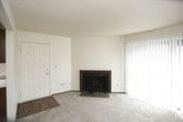 This single-floor unit offers a functional and straightforward layout with several notable features throughout. The living area is carpeted and anchored by a brick fireplace with a metal surround, adding a classic focal point to the space. A ceiling fan overhead provides practical comfort, while an open passageway connects the living room directly to the kitchen. A sliding glass door in an adjacent room floods the space with natural light through vertical blinds, creating a bright and open atmosphere.

The galley-style kitchen is equipped with dark wood cabinetry above and below white laminate countertops, offering ample storage. White appliances, including a refrigerator, electric range, and dishwasher, line one wall, while a stainless steel sink is positioned along the opposite counter. Wood-look flooring runs through the kitchen, adding warmth to the space.

The bedroom is generously sized with plush carpeting, a textured ceiling, a window with a view to the outside, and access to a walk-in closet and a private bathroom. The bathroom features wood-look flooring, a full tub-shower combination, a toilet, and a vanity with a wood-framed mirror and integrated sink.