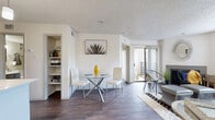 This single-story, one-bedroom, one-bathroom unit offers a thoughtfully designed layout across a compact yet efficiently utilized floor plan. Dark hardwood-style flooring runs consistently throughout all rooms, providing a cohesive and polished aesthetic.

The living room serves as the heart of the space, featuring a fireplace, a large window that allows generous natural light, and a sliding glass door opening to a private outdoor area. A defined dining area adjacent to the living room benefits from a second sliding glass door, further enhancing natural light and outdoor access. An open shelving unit nearby provides convenient additional storage.

The kitchen is well-equipped with gray cabinetry, quartz countertops, a mosaic tile backsplash, stainless steel appliances, a double-basin sink, and dark flooring. Notably, an in-unit washer is conveniently located just off the kitchen.

The bedroom is comfortably sized, featuring a ceiling fan, a sliding glass door to an outdoor balcony area, and direct access to a spacious walk-in closet with wrap-around hanging rods.

The bathroom includes a single-sink vanity with gray cabinetry, a framed mirror, and a full tub-shower combination with tile surround.