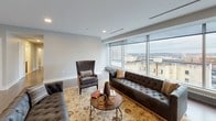 This single-floor urban residence combines contemporary design with functional living across a well-organized layout. The expansive living area serves as the centerpiece of the space, anchored by dramatic floor-to-ceiling windows that frame sweeping city skyline views and flood the interior with natural light. Hardwood flooring in a warm medium-tone finish runs throughout the main living areas, lending continuity and warmth to the space.

The kitchen is thoughtfully designed with dark espresso-stained cabinetry extending to the ceiling, providing generous storage. Granite countertops, a subway tile backsplash, and a full suite of stainless steel appliances—including a French door refrigerator, range, and microwave—deliver a polished, functional workspace. A large island with seating for two serves as an informal dining and gathering area, accented by pendant lighting overhead.

The bedroom areas feature neutral gray walls, recessed lighting, and hardwood floors, with select rooms benefiting from their own city-facing windows. The bathroom is finished with large-format light tile flooring, a dark-toned vanity, and clean-lined modern fixtures, accompanied by a walk-in closet with built-in shelving. Recessed lighting throughout maintains a refined, contemporary ambiance.