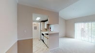 This single-story, one-bedroom, one-bathroom unit offers a practical and efficient layout designed to maximize its compact footprint. The entry opens into a living area finished with neutral-toned carpet and accented by crown molding details. A ceiling fan with a light fixture provides both airflow and ambient lighting, while a large window fitted with blinds and a private exterior door fill the space with natural light and offer convenient outdoor access.

The kitchen is positioned at the heart of the unit, separated from the living area by a peninsula-style breakfast bar that provides additional counter space and a visual divider. The galley-style kitchen features light wood cabinetry, white appliances including a range, refrigerator, dishwasher, and microwave, along with a built-in sink. Light tile flooring runs throughout the kitchen, contrasting with the carpeted living spaces. A skylight overhead brightens the cooking area naturally.

The bathroom is cleanly appointed with white tile surrounding a full tub-shower combination, a vanity with a sink, a large mirror, and tile flooring. The neutral, light color palette carried throughout the unit creates a cohesive, open ambiance well-suited for comfortable everyday living.