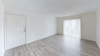 This single-floor unit offers a practical and well-maintained layout designed for comfortable everyday living. The living area is bright and open, featuring light gray wood-look flooring and a sliding glass door with vertical blinds that invites natural light and provides outdoor access. Adjacent to the living space is a dining or secondary living area, also with light wood-look flooring and a ceiling fan with light fixture overhead.

The galley-style kitchen is efficiently laid out with white cabinetry, light countertops, a stainless steel sink, and a tile backsplash. White appliances including a refrigerator, electric range, and microwave are included, with light wood-look flooring tying the space together.

The bedrooms feature neutral carpet and bright white walls, offering a clean and versatile canvas. Each room benefits from natural light through windows with blinds, and ceiling fixtures or ceiling fans provide overhead lighting and airflow.

The bathroom is straightforward and functional, with a shower/tub combination, a toilet, and a single vanity with a light countertop and white cabinetry. A large mirror with a lighted vanity bar above adds brightness to the space. Throughout the unit, the consistent white walls, neutral flooring, and clean finishes create a cohesive and move-in-ready environment.