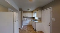 This 2-floor space includes a kitchen that showcases a straightforward, functional design. The kitchen is outfitted with white cabinetry arranged in an L-shaped configuration, providing ample storage along the upper and lower walls. White appliances include a freestanding electric range, a dishwasher, and a full-sized refrigerator, offering a complete and cohesive look. A double-basin sink is positioned beneath a window, allowing natural light to filter into the space. The countertops feature a light neutral tone that complements the white cabinetry, while the flooring consists of a durable tile with a warm, earthy pattern. The walls are finished in a taupe-grey tone, adding a subtle contrast against the white elements. Overhead, flush-mount light fixtures provide consistent illumination throughout the kitchen. The overall ambiance of the kitchen is practical and clean, designed with usability in mind. Spanning two floors, the full space offers additional rooms and living areas beyond what is visible, providing a multi-level layout suited for comfortable everyday living.