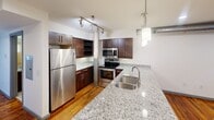 This 770 square foot apartment in Charlotte, NC spans two floors, with 570 sq ft on the main level and 190 sq ft upstairs. The modern kitchen boasts dark wood cabinetry, granite countertops, and stainless steel appliances, including a side-by-side refrigerator and built-in microwave. The bathroom features a granite vanity and a large, white tiled shower with a curved rod. Industrial-chic elements like exposed ductwork and pendant lighting complement the warm hardwood floors throughout. The open layout and thoughtful design maximize the use of space in this compact yet stylish urban dwelling.