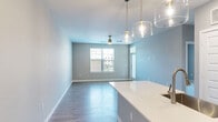 This well-appointed single-floor residence offers a clean, modern aesthetic highlighted by a cohesive neutral color palette and quality finishes throughout. The open-concept living and dining area is anchored by light gray walls, smooth hardwood-style flooring, and a stylish ceiling fan with a brushed gold fixture. Elegant glass pendant lights hang over the kitchen island, which features a crisp white countertop that seamlessly connects to the main living space. Natural light flows in through multiple windows fitted with horizontal blinds, creating a bright and airy atmosphere.

The kitchen is equipped with stainless steel appliances, including a refrigerator, electric range, and over-the-range microwave, all complemented by white shaker-style cabinetry and a subtle gray tile backsplash. A built-in entryway nook with hooks provides a practical drop zone near the entrance.

The bedrooms are carpeted in soft neutral tones and outfitted with ceiling fans, offering a comfortable and quiet retreat. Each room benefits from natural light via exterior-facing windows. The full bathroom is elegantly finished with white cabinetry, a quartz vanity countertop, a large frameless glass-enclosed shower-tub combination with tile surround, and brushed nickel hardware throughout.