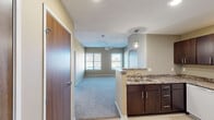 Located in Cedar Rapids, Iowa, this single-floor unit offers a practical and comfortable layout designed for everyday living. The open-concept kitchen and living area serves as the heart of the space, where rich dark-wood cabinetry, granite-style countertops, a kitchen island with pendant lighting, and white GE appliances — including an electric range, over-the-range microwave, dishwasher, and refrigerator — combine for a functional cooking environment. Light hardwood-style flooring runs through the kitchen and entry area, while plush carpet extends into the living room, which features a ceiling fan and windows that bring in natural light. The bedrooms are generously sized with soft carpeting, ceiling fans, and ample closet space — including a spacious walk-in closet outfitted with an adjustable wire shelving system. A secondary bedroom also features built-in closet storage. Two bathrooms serve the unit: one with a tub/shower combination, a vanity with white countertop, and a large mirror, and another with a single-sink vanity and tile-style flooring. Throughout, warm neutral wall tones, textured ceilings, and consistent dark-wood door finishes create a cohesive and inviting aesthetic.