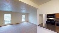 This single-floor residence offers a practical and functional layout across several well-defined living spaces. The living area is open and inviting, featuring soft carpet flooring, neutral wall tones, and a window that allows natural light to filter in. A textured ceiling adds subtle character to the space, while a granite-topped counter peninsula connects the living area to the kitchen, providing a convenient pass-through and additional surface space.

The galley-style kitchen is efficiently designed with warm honey-toned wood cabinetry lining both walls, dark granite countertops, hardwood flooring, and black appliances including a range, dishwasher, and full-size refrigerator. A double basin sink is positioned beneath upper cabinetry, maximizing storage and workspace throughout.

The unit includes multiple bedrooms, each finished with plush carpet and neutral walls. The primary bedroom benefits from dual windows that bring in ample natural light and offer views of the surrounding exterior. Additional bedrooms are well-proportioned and versatile.

The bathroom features a full tub and shower combination with white tile surround and brushed nickel fixtures, complemented by a separate water closet with tile flooring for added privacy. The overall floor plan, as seen in the dollhouse view, reflects a thoughtful arrangement of interconnected spaces designed for comfortable everyday living.