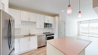 Located at 10 Westedge St in Charleston, SC, this well-appointed 1-bedroom, 2-bathroom residence offers a thoughtfully designed single-level layout with a clean, contemporary aesthetic throughout. Light wood-tone flooring flows seamlessly through the living, dining, and bedroom areas, complementing the neutral warm-white palette that gives the space a bright, cohesive feel.

The kitchen is a standout feature, showcasing white shaker cabinetry extending to the ceiling, a herringbone-patterned tile backsplash, and a full suite of stainless steel appliances including a refrigerator, range, microwave, and dishwasher. A central island with a soft blush countertop provides additional prep and dining space, while pendant lighting with warm-toned glass shades adds an inviting accent.

The living area offers an open, airy feel with a glazed door providing natural light and access to an outdoor area, along with views of the Charleston cityscape. The bedroom is a comfortable, well-proportioned retreat equipped with a ceiling fan, large window with city views, and access to a dedicated closet.

Both bathrooms are finished with large-format light tile flooring, white vanity cabinetry, and clean fixtures. The primary bath features a glass-enclosed walk-in shower with white tile surround and a single-sink vanity with ample storage.