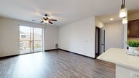 This well-designed single-floor residence offers a clean, modern aesthetic throughout its open-concept layout. The expansive living area is finished with wood-look plank flooring, dark baseboards, and a ceiling fan with light fixture, creating a bright and airy atmosphere. Sliding glass doors lead to a private balcony, filling the space with natural light and offering outdoor views.

The kitchen is a standout feature, boasting rich dark-toned cabinetry, light quartz countertops, and a full suite of stainless steel appliances including a refrigerator, range, microwave, and dishwasher. A central island with pendant lighting adds both workspace and a visual focal point, seamlessly connecting the kitchen to the living area. Track lighting provides additional illumination.

The bedroom is carpeted for comfort and includes access to a generously sized walk-in closet outfitted with wire shelving systems for organized storage. The primary bathroom impresses with a dual-sink vanity, dark cabinetry, quartz countertops, framed mirrors, and a glass-enclosed shower.

Practical amenities include an in-unit laundry closet equipped with a front-loading washer and dryer. The cohesive use of dark trim, neutral tones, and modern finishes gives the entire space a polished, contemporary character.