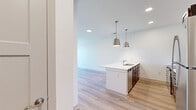 This 1-bedroom, 1-bathroom unit in McCordsville, Indiana offers a thoughtfully planned layout across a single floor. The open-concept kitchen and living area serves as the heart of the home, featuring light wood-style flooring, crisp white walls, and recessed lighting throughout. The kitchen is well-appointed with dark espresso cabinetry, white quartz countertops, a peninsula with an undermount sink, stainless steel appliances—including a refrigerator, electric range, and microwave—and a light blue subway tile backsplash. Stylish pendant lights hang above the peninsula, adding a modern touch. The living area provides a bright, open canvas with ample natural light from large windows. The bedroom is carpeted for comfort, includes a ceiling fan, and offers access to a generously sized walk-in closet outfitted with wire shelving systems. The full bathroom features dark wood vanity cabinetry, white countertops, and a fully tiled walk-in shower with a handheld showerhead. A dedicated laundry area houses a stacked washer and dryer unit alongside a water heater, keeping utilities efficiently organized. Clean lines and neutral tones throughout create a cohesive, contemporary atmosphere.