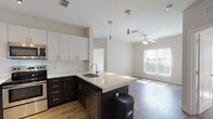 This well-designed single-floor residence offers a clean, contemporary aesthetic throughout. The heart of the home is an open-concept kitchen that flows seamlessly into the living area. The kitchen is outfitted with a striking two-tone cabinetry scheme — dark espresso lower cabinets paired with crisp white upper cabinets — and complemented by quartz countertops and a matching kitchen island with an integrated sink. A full suite of stainless steel appliances, including a range, microwave, refrigerator, and dishwasher, completes the culinary space. Warm hardwood-style flooring extends through the kitchen and living areas, while pendant and track lighting add both style and function. The living area benefits from natural light through a large window and is finished with a ceiling fan overhead. The bedrooms are carpeted for comfort, each featuring ceiling fans and multiple windows dressed with vertical blinds that invite abundant natural light. Two bathrooms serve the residence: one with a tub-shower combination and the other with a sleek glass-enclosed walk-in shower. Both bathrooms feature wood-style flooring and dark vanity cabinetry. The overall palette of neutral tones and modern finishes creates a bright, cohesive, and move-in-ready living environment.