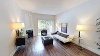 Located at 7047 Alvern St in the Westchester neighborhood of Los Angeles, this single-story residence offers a well-appointed layout with thoughtfully designed living spaces throughout. The living room serves as the heart of the home, showcasing rich, dark hardwood flooring that extends throughout the main areas. A classic fireplace with a white surround and decorative built-in niche above anchors one wall, while a large sliding glass door floods the space with natural light and provides direct access to an outdoor area with greenery views, creating a seamless indoor-outdoor connection.

Adjacent to the living room, the dining area features a mirrored wall that amplifies natural light and gives the space an open, expansive feel. A pendant chandelier adds an elegant focal point above the dining space. The kitchen is outfitted with dark espresso cabinetry, crisp white countertops, and stainless steel appliances including a gas range and built-in microwave, offering a sleek, contemporary aesthetic.

The bedroom is carpeted for comfort and includes built-in dark wood cabinetry for additional storage. Natural light filters in through a window, contributing to the room's calm, restful atmosphere. Textured ceilings are present throughout, and the overall color palette of soft neutrals creates a cohesive, inviting ambiance across the entire home.