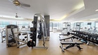 Located at 301 E North Water St in Chicago's Streeterville neighborhood, this fitness center offers a thoroughly equipped workout facility designed to accommodate a full range of exercise needs. The space is laid out across a single level, with distinct zones dedicated to cardiovascular training and strength work.

The cardio area features a row of modern treadmills, elliptical trainers, and stair climbers aligned along floor-to-ceiling windows, providing unobstructed views of the Chicago skyline and waterfront. A mounted flat-screen television accompanies the cardio zone, enhancing the workout experience. The natural light from the expansive windows creates a bright and energizing atmosphere throughout the facility.

The strength training section is well-stocked with cable machines, multi-functional weight stations, adjustable benches, and a comprehensive rack of Matrix-branded dumbbells. The layout allows ample space for movement between equipment. Large mirrors along one wall visually expand the space and assist with form during exercises.

Near the entrance, built-in cabinetry with open shelving stocks fresh towels, and a water station is conveniently positioned for use. The flooring throughout is a durable speckled rubber composite, and a tray ceiling with warm accent lighting adds a polished architectural detail to the overall design.