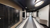 Located at 1000 SW Vista Ave in Portland, Oregon, this single-floor amenity space is designed with a consistent modern aesthetic characterized by dark ceilings with exposed elements, bold black-and-white striped flooring, and recessed lighting throughout. The layout extends along a central corridor flanked by distinct functional areas, each serving a specific resident need.

The mail and entry corridor sets the tone with its striking tile flooring, rows of numbered mailboxes mounted along textured accent walls, pendant lighting, and a seating bench for convenience. The design creates a structured, organized arrival experience.

The fitness center is well-equipped with cardio machines including treadmills, stationary bikes, and a rowing machine, alongside free weights, a cable machine, and a weight bench. Full-length mirrors amplify the space, and a drop ceiling with recessed panel lighting provides even illumination. A separate area accommodates additional cardio equipment and a wall-mounted fan for ventilation.

The community lounge features an open-ceiling design with exposed ductwork painted black, a central dining table with modern chairs, a bookshelf stocked with reading materials, and a dedicated ironing station, creating a versatile multipurpose space.

The laundry facility includes multiple commercial-grade front-loading washers, stacked dryer units, folding tables, a utility sink, and an illuminated neon "Laundry" sign, lending a clean and functional environment with an intentional design touch.