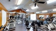 Located at 100 Eclipse Dr in Cary, North Carolina, this fitness center offers a well-appointed workout space designed to support a full range of exercise routines. The single-floor facility features vaulted ceilings with a classic angled roofline, giving the space an open and airy feel. Ceiling fans are strategically placed throughout to maintain comfortable airflow during workouts.

The gym is outfitted with a variety of cardio equipment, including treadmills and elliptical machines from reputable brands such as TRUE Fitness, alongside a comprehensive selection of strength training machines and free weight stations. Full-length mirrors line the walls, enhancing the sense of space while allowing users to monitor their form during exercise.

Natural light filters in through the windows, complemented by recessed skylight-style fixtures in the ceiling, keeping the environment bright and energizing throughout the day. The warm earth-toned accent walls add a vibrant, motivating atmosphere to the space. The durable flooring is well-suited for high-traffic fitness use. Overall, this fitness center provides a functional, well-lit, and thoughtfully designed environment for residents looking to maintain an active lifestyle.