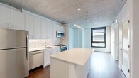 Located at 918 W School St in Chicago's sought-after Lakeview neighborhood, this one-bedroom, one-bathroom unit offers a thoughtfully designed layout with contemporary finishes throughout. The open-concept kitchen and living area serves as the heart of the unit, showcasing an exposed concrete ceiling that lends an industrial character to the space. The kitchen is well-appointed with sleek white cabinetry, a hexagonal tile backsplash, stainless steel appliances including a gas range, built-in microwave, dishwasher, and refrigerator, and a central island with a clean white countertop ideal for dining or meal prep. Linear pendant lighting above the island adds a modern touch. Rich hardwood flooring runs throughout the main living areas, complementing the bright white walls. The bedroom features the same exposed concrete ceiling, a large window that allows natural light to filter in, and direct access to a dedicated closet with built-in shelving. A second closet and an in-unit laundry area provide additional storage and convenience. The bathroom is finished with white subway tile surrounding a soaking tub and shower combo, marble-look flooring, and chrome fixtures, creating a clean, spa-like atmosphere. This unit combines industrial design elements with modern comforts in a compact, efficient floor plan.