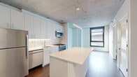 Located at 918 W School St in Chicago's sought-after Lakeview neighborhood, this one-bedroom, one-bathroom unit offers a thoughtfully designed layout with contemporary finishes throughout. The open-concept kitchen and living area serves as the heart of the unit, showcasing an exposed concrete ceiling that lends an industrial character to the space. The kitchen is well-appointed with sleek white cabinetry, a hexagonal tile backsplash, stainless steel appliances including a gas range, built-in microwave, dishwasher, and refrigerator, and a central island with a clean white countertop ideal for dining or meal prep. Linear pendant lighting above the island adds a modern touch. Rich hardwood flooring runs throughout the main living areas, complementing the bright white walls. The bedroom features the same exposed concrete ceiling, a large window that allows natural light to filter in, and direct access to a dedicated closet with built-in shelving. A second closet and an in-unit laundry area provide additional storage and convenience. The bathroom is finished with white subway tile surrounding a soaking tub and shower combo, marble-look flooring, and chrome fixtures, creating a clean, spa-like atmosphere. This unit combines industrial design elements with modern comforts in a compact, efficient floor plan.