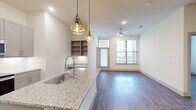 This thoughtfully designed two-bedroom, two-bathroom residence combines modern aesthetics with functional living across a single floor. The open-concept kitchen serves as the heart of the home, featuring granite countertops, a large center island with an undermount sink, gray shaker-style cabinetry, stainless steel appliances, a tile backsplash, and striking geometric pendant lighting. Wood-look flooring flows seamlessly from the kitchen into the living area, which is bathed in natural light from large windows and accented by a ceiling fan overhead. Built-in shelving adds a practical decorative touch near the main living space. The primary bedroom is generously sized and connects to a spacious en-suite bathroom with a dual-sink granite vanity, marble-look tile flooring, and a walk-in shower. A large walk-in closet with multi-level shelving and hanging rods provides exceptional storage. The second bathroom features the same elegant marble-look tile, a soaking tub with a tiled surround, and a granite vanity. The second bedroom offers wood-look flooring and a bright window with outdoor views. Clean white walls and recessed lighting throughout create a bright, cohesive ambiance across the entire residence.