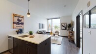Located at 4018 N Williams Ave in Portland's vibrant Williams Avenue corridor, this contemporary unit offers a well-designed open-concept layout with modern finishes throughout. The kitchen is a standout feature, equipped with stainless steel appliances including a gas range, microwave, and refrigerator, complemented by dark espresso cabinetry, light quartz countertops, and a peninsula island with bar seating — ideal for casual dining or entertaining. A pendant light adds a refined touch overhead. The living area flows seamlessly from the kitchen, bathed in abundant natural light from dramatic floor-to-ceiling windows that frame views of the surrounding Portland neighborhood. Dark hardwood-style flooring runs throughout, grounding the bright, white walls and creating a cohesive, modern aesthetic. The bedroom is a calm retreat featuring its own floor-to-ceiling window with city views, ample closet space with sliding doors, and room for a generous bed. The bathroom is clean and functional, offering a full tub-shower combination with wood-style flooring. An in-unit stacked washer and dryer provides added convenience. The overall ambiance is contemporary and urban, reflecting the energy and character of Portland's dynamic North Williams neighborhood.