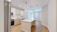 Located at 10149 Arise Loop in Orlando, Florida, this thoughtfully designed one-bedroom, one-bathroom residence offers a well-appointed open-concept living space across a single floor. Light wood-tone flooring flows throughout the main living areas, creating a warm, cohesive aesthetic. The kitchen is a standout feature, boasting white upper cabinetry paired with natural wood-toned lower cabinets, a white subway tile backsplash, stainless steel appliances, and a central island with a clean quartz countertop illuminated by modern pendant lighting. The kitchen opens seamlessly into the dining and living areas, which are brightened by natural light from large windows and finished with a ceiling fan overhead. The spacious primary bedroom features plush carpeting, generous natural light, and access to a walk-in closet with built-in wire shelving. Additional closet space adds to the home's ample storage. The full bathroom includes a combination tub and shower, a wood-toned vanity, and light flooring that mirrors the home's modern palette. A dedicated laundry area and a private balcony with a storage unit complete the residence. The balcony overlooks the building's exterior, providing a pleasant outdoor retreat.