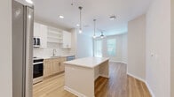 Located at 10149 Arise Loop in Orlando, Florida, this thoughtfully designed one-bedroom, one-bathroom residence offers a well-appointed open-concept living space across a single floor. Light wood-tone flooring flows throughout the main living areas, creating a warm, cohesive aesthetic. The kitchen is a standout feature, boasting white upper cabinetry paired with natural wood-toned lower cabinets, a white subway tile backsplash, stainless steel appliances, and a central island with a clean quartz countertop illuminated by modern pendant lighting. The kitchen opens seamlessly into the dining and living areas, which are brightened by natural light from large windows and finished with a ceiling fan overhead. The spacious primary bedroom features plush carpeting, generous natural light, and access to a walk-in closet with built-in wire shelving. Additional closet space adds to the home's ample storage. The full bathroom includes a combination tub and shower, a wood-toned vanity, and light flooring that mirrors the home's modern palette. A dedicated laundry area and a private balcony with a storage unit complete the residence. The balcony overlooks the building's exterior, providing a pleasant outdoor retreat.